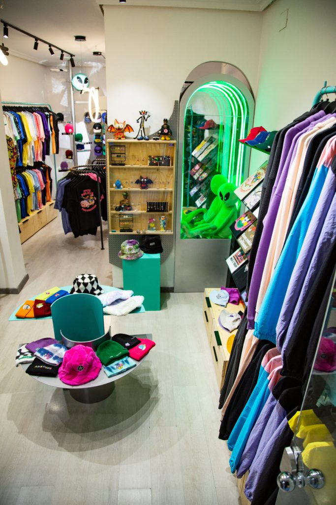 Interior de la tienda Aristicos con prendas de diseño y un espejo iluminado en verde